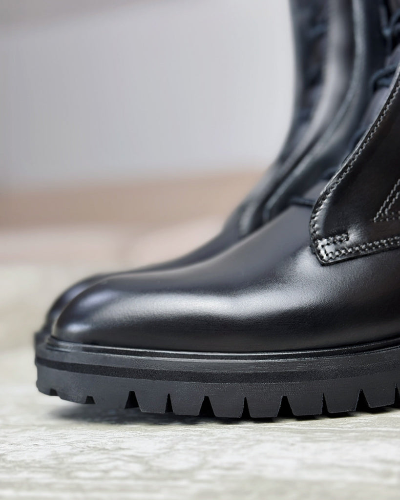 Close-up of a black boot with a textured sole on a light background