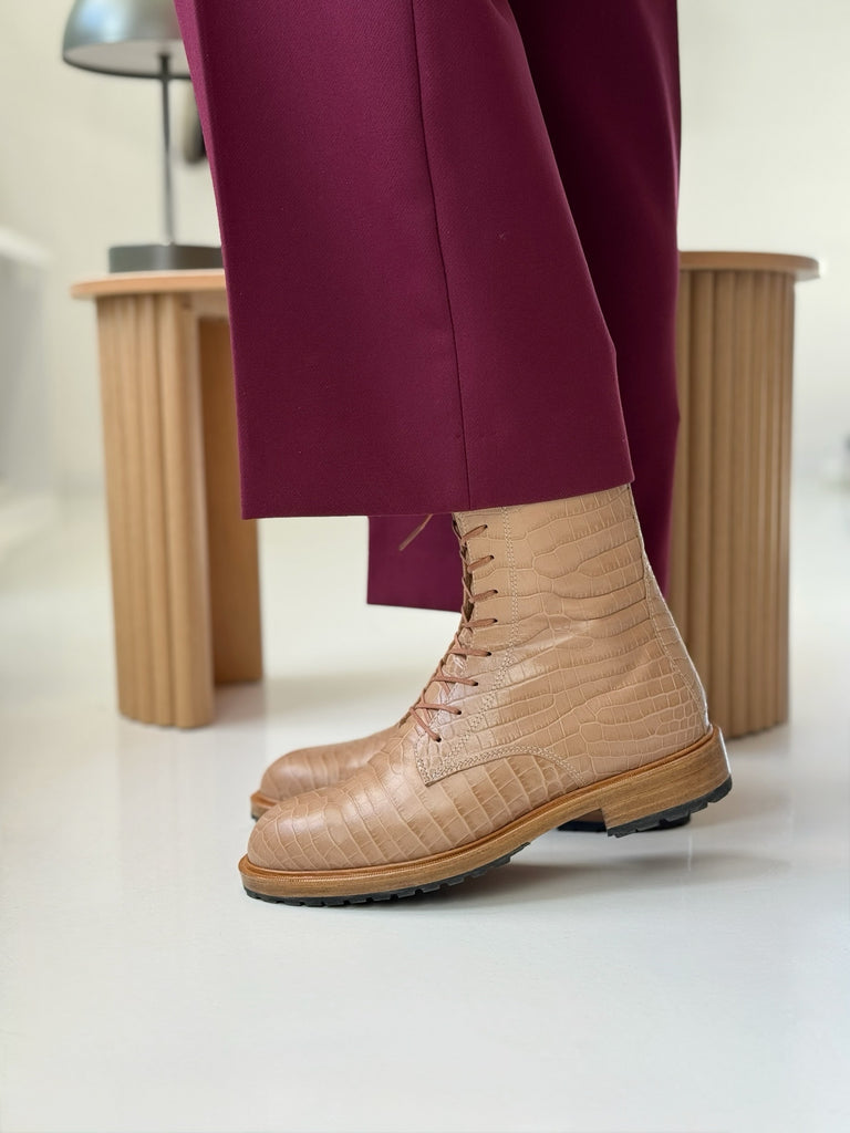 Beige lace-up croco boots worn with burgundy pants on a light background